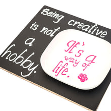 a white plate with pink writing on it with text: 'Being creative is not a a way of hobby. life.'